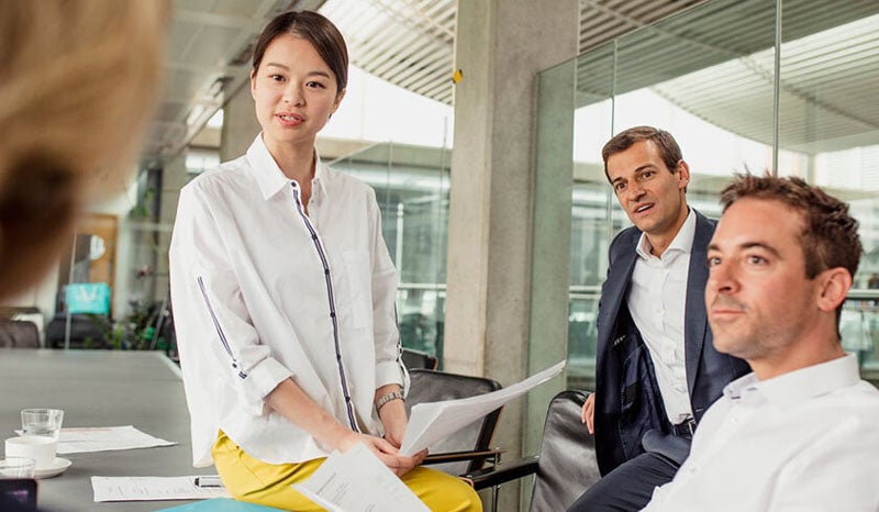 A woman standing in front of colleagues, leading a business discussion in an office.