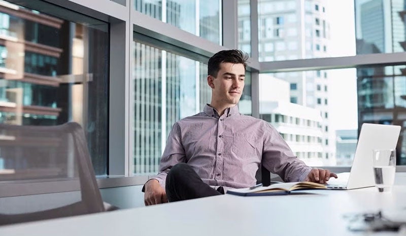 A man sitting comfortably at a desk working on his laptop in a modern office.