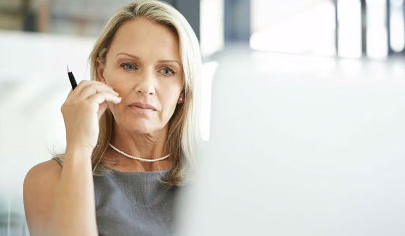 A woman deep in thought while working at her desk in the office.